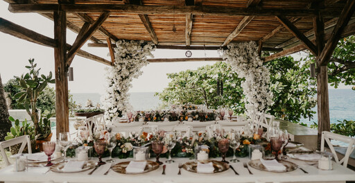 Tische für Hochzeitsmahl gedeckt, draußen mit Überdachung, im Hintergrund das Meer